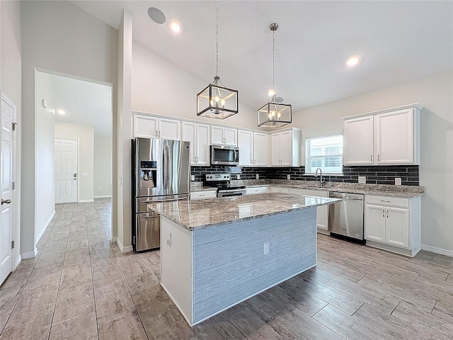 kitchen with a center island, hanging light fixtures, light stone countertops, appliances with stainless steel finishes, and white cabinets