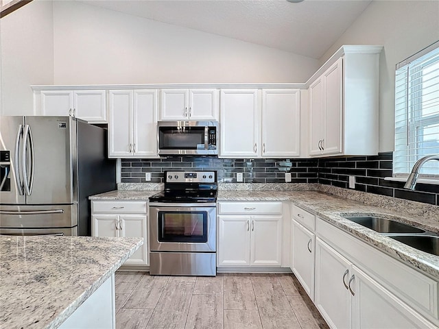 kitchen featuring vaulted ceiling, sink, appliances with stainless steel finishes, white cabinets, and light stone counters