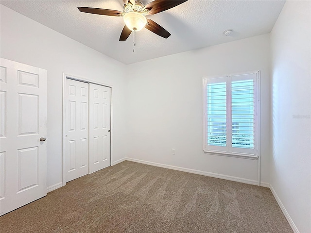 unfurnished bedroom featuring ceiling fan, a textured ceiling, a closet, and carpet floors