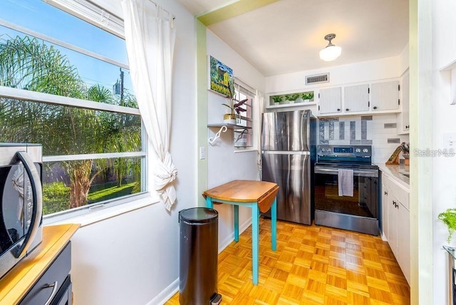 kitchen featuring white cabinets, backsplash, appliances with stainless steel finishes, and light parquet floors