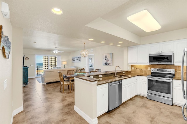 kitchen featuring kitchen peninsula, sink, white cabinetry, stainless steel appliances, and ceiling fan with notable chandelier