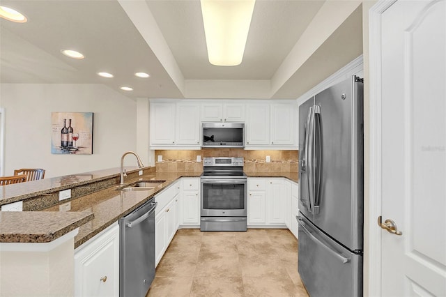 kitchen with kitchen peninsula, sink, stainless steel appliances, white cabinets, and dark stone counters