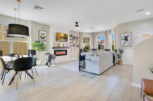 living room with ceiling fan, a large fireplace, and light wood-type flooring