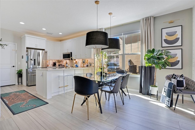 kitchen with appliances with stainless steel finishes, backsplash, white cabinets, light hardwood / wood-style floors, and hanging light fixtures