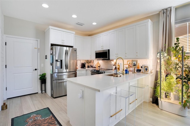 kitchen featuring kitchen peninsula, backsplash, stainless steel appliances, sink, and white cabinetry