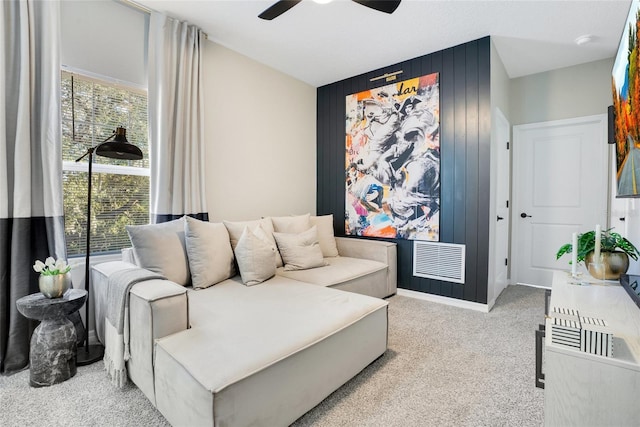 carpeted living room with ceiling fan and wood walls