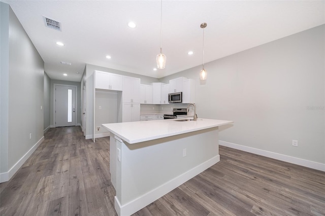 kitchen featuring pendant lighting, an island with sink, hardwood / wood-style floors, white cabinetry, and appliances with stainless steel finishes