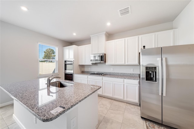 kitchen with a center island with sink, appliances with stainless steel finishes, light stone counters, white cabinets, and sink