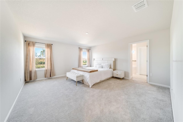 unfurnished bedroom with ensuite bath, a textured ceiling, light carpet, and multiple windows