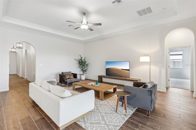 living room with ceiling fan, a tray ceiling, and crown molding