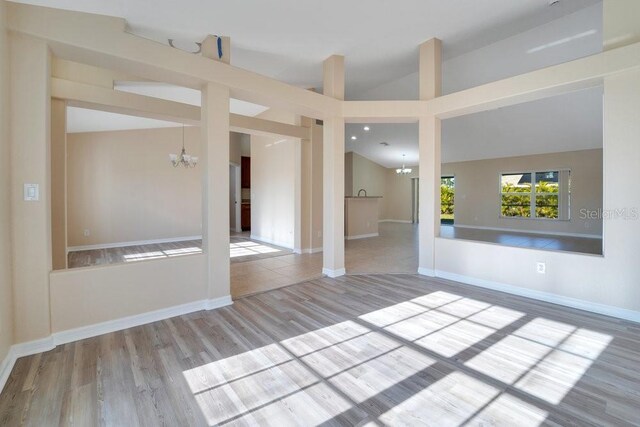 unfurnished living room with a notable chandelier, light hardwood / wood-style floors, and vaulted ceiling