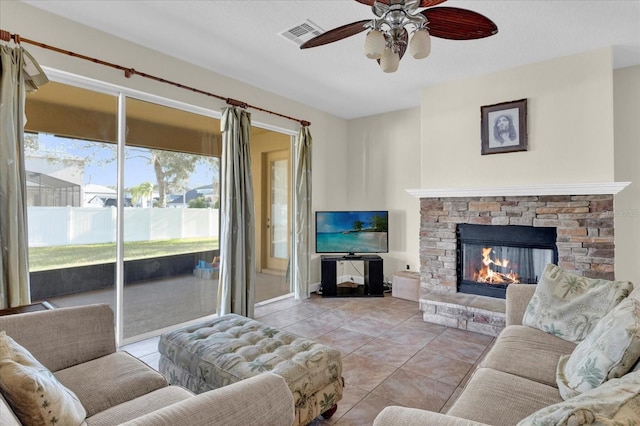 tiled living room featuring ceiling fan and a stone fireplace