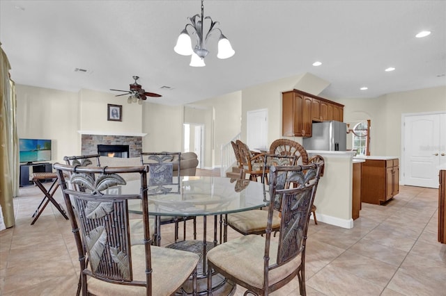 tiled dining room with ceiling fan with notable chandelier and a fireplace