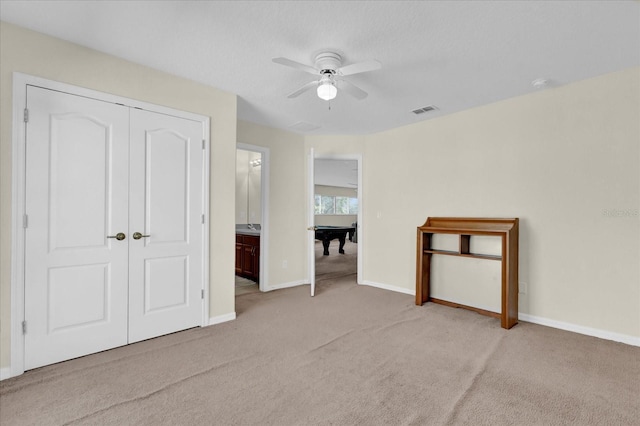 interior space featuring ceiling fan, a closet, ensuite bathroom, and light carpet