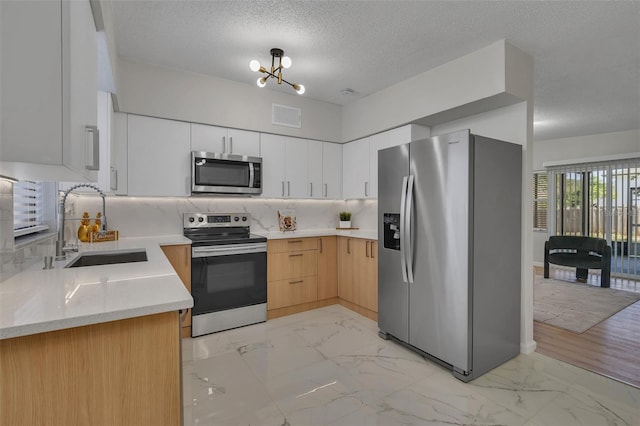 kitchen featuring decorative backsplash, appliances with stainless steel finishes, sink, a notable chandelier, and white cabinetry