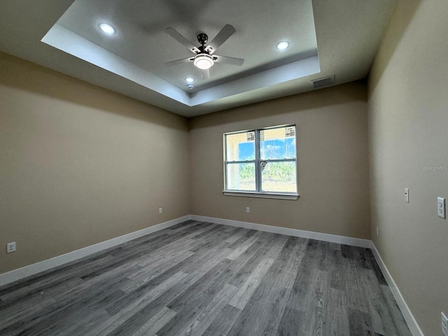 empty room featuring a tray ceiling, baseboards, visible vents, and ceiling fan