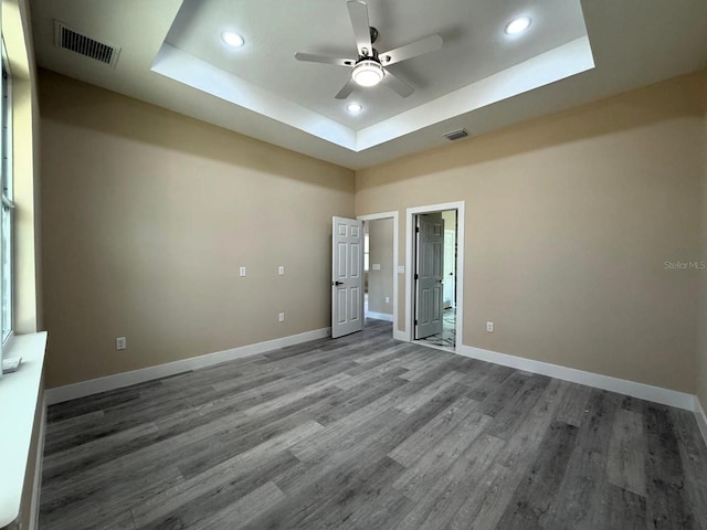 empty room with visible vents, a raised ceiling, wood finished floors, and a ceiling fan