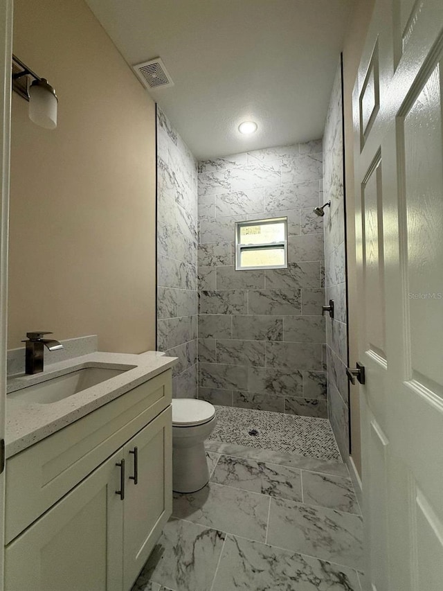 full bathroom featuring visible vents, toilet, tiled shower, marble finish floor, and vanity