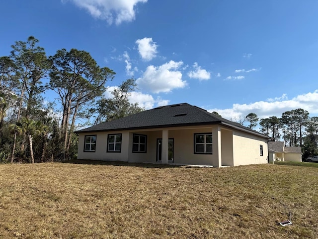 back of property with stucco siding, a yard, and a shingled roof