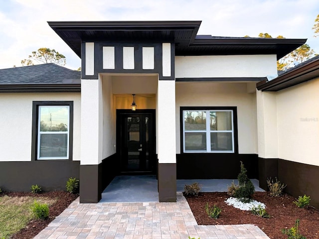 entrance to property featuring a shingled roof and stucco siding