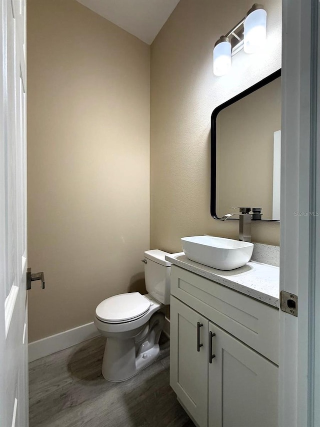 half bath featuring baseboards, toilet, wood finished floors, and vanity