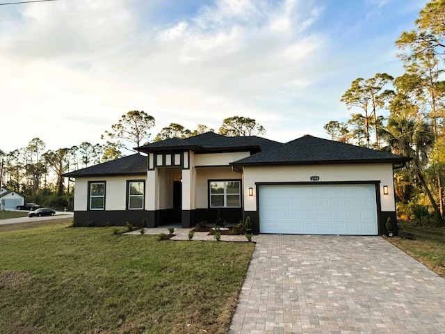 prairie-style house featuring a front yard, decorative driveway, an attached garage, and stucco siding