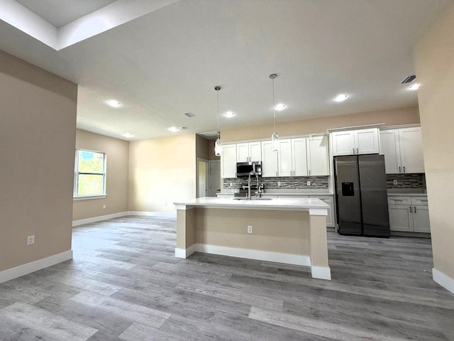 kitchen with baseboards, a kitchen island with sink, stainless steel appliances, decorative backsplash, and light countertops