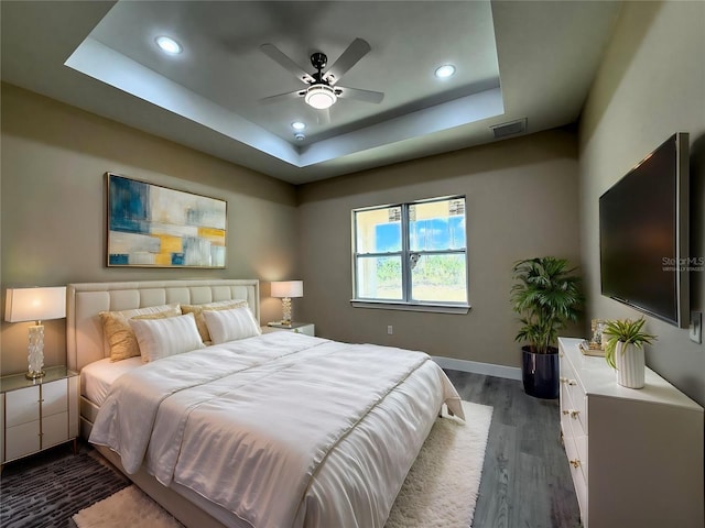 bedroom with wood finished floors, visible vents, baseboards, recessed lighting, and a raised ceiling