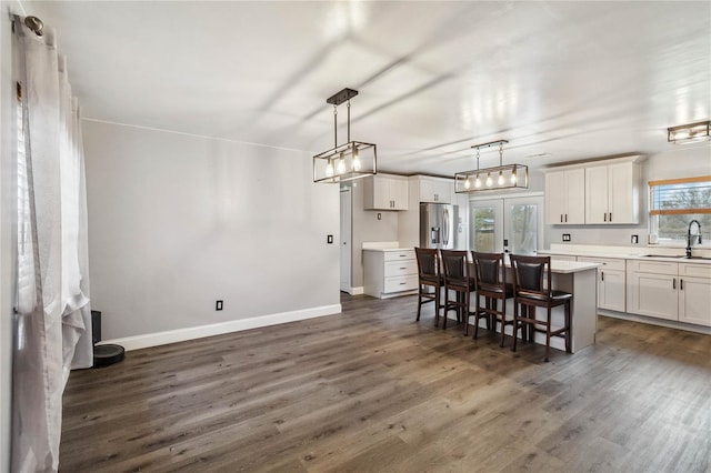 kitchen featuring a kitchen bar, a center island, stainless steel fridge with ice dispenser, hanging light fixtures, and white cabinets