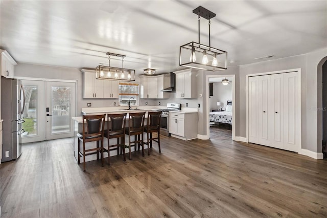 kitchen featuring wall chimney exhaust hood, stainless steel appliances, hanging light fixtures, and white cabinets