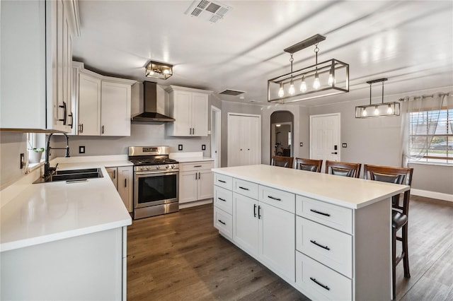 kitchen with wall chimney range hood, gas range, sink, and a kitchen island