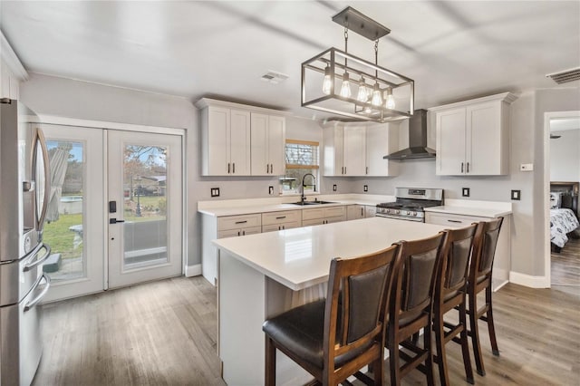 kitchen with appliances with stainless steel finishes, white cabinetry, sink, a center island, and wall chimney range hood