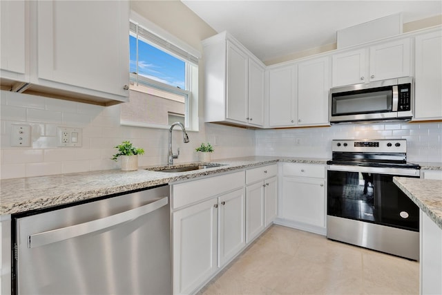 kitchen with light stone countertops, white cabinetry, stainless steel appliances, sink, and backsplash