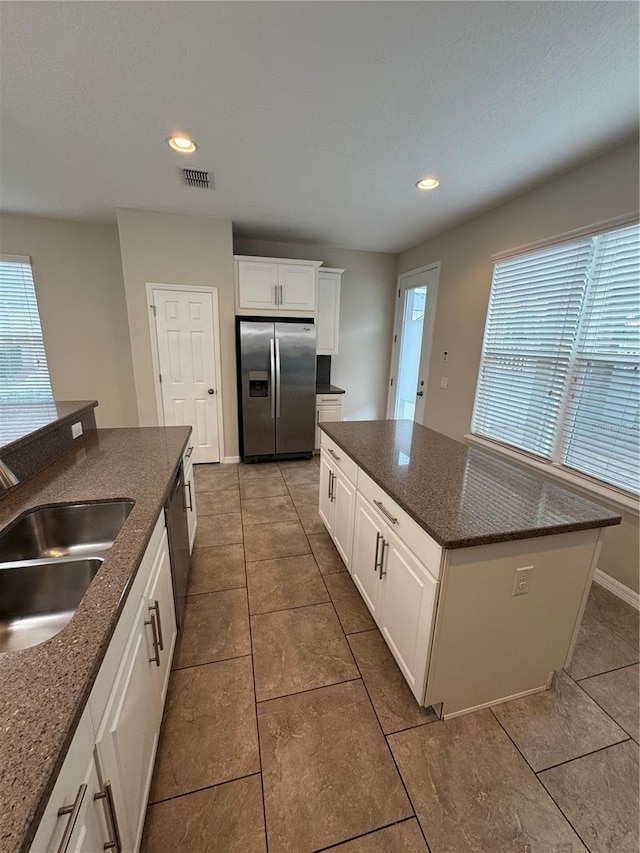 kitchen featuring stainless steel fridge, tile patterned floors, a kitchen island, sink, and white cabinetry