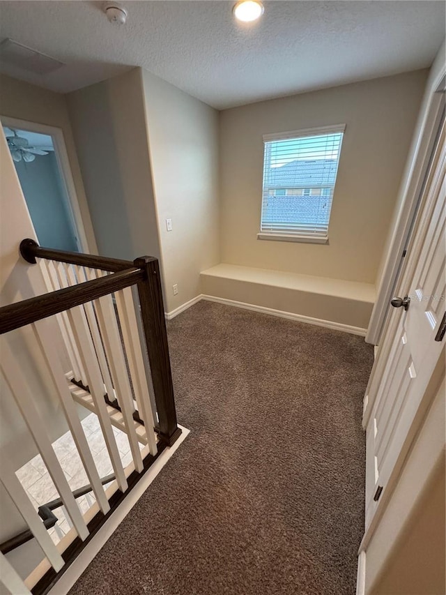 hallway with dark carpet and a textured ceiling