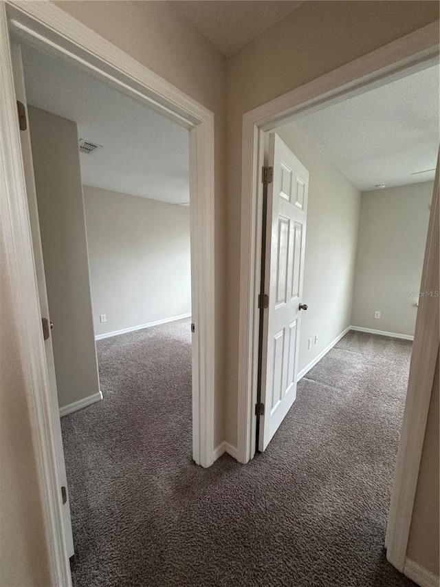 hall with dark colored carpet and a textured ceiling