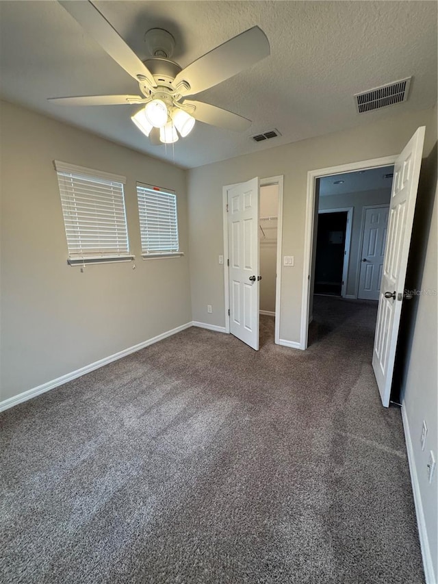 unfurnished bedroom with dark colored carpet, a closet, a spacious closet, and ceiling fan