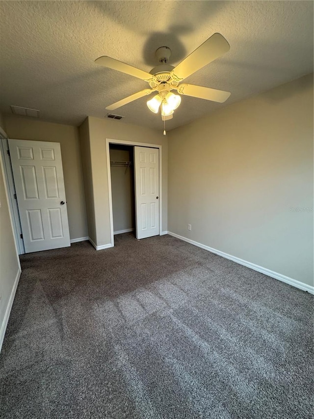 unfurnished bedroom with dark colored carpet, ceiling fan, a textured ceiling, and a closet