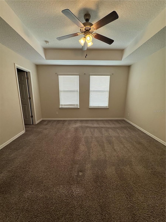 empty room with dark colored carpet, ceiling fan, and a tray ceiling