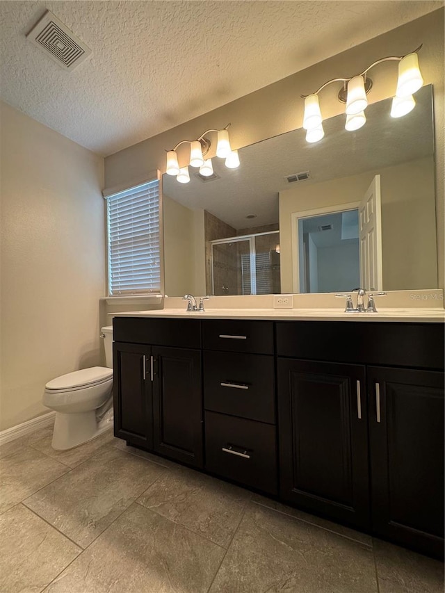 bathroom with a textured ceiling, vanity, toilet, and a shower with door