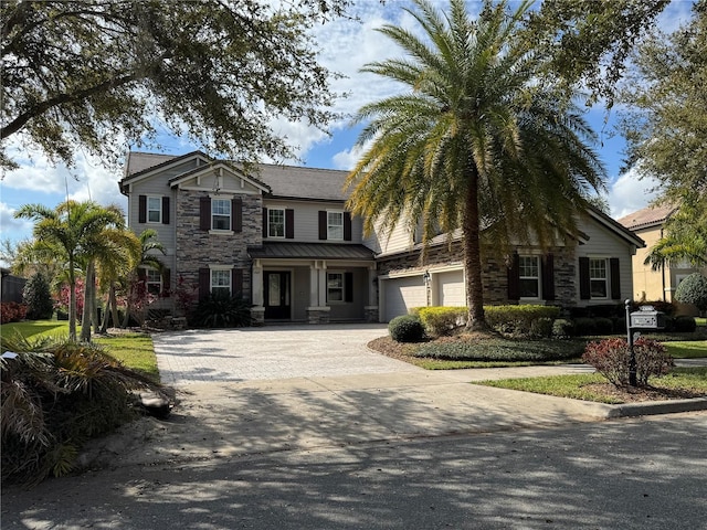 view of front facade with metal roof, stone siding, decorative driveway, and an attached garage