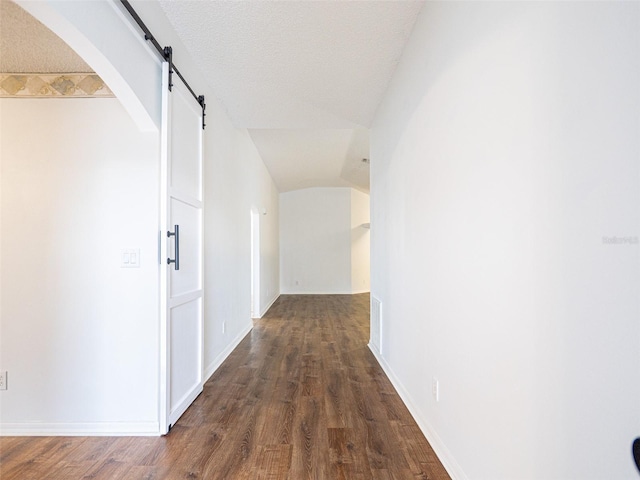 hall featuring a barn door, vaulted ceiling, dark hardwood / wood-style flooring, and a textured ceiling