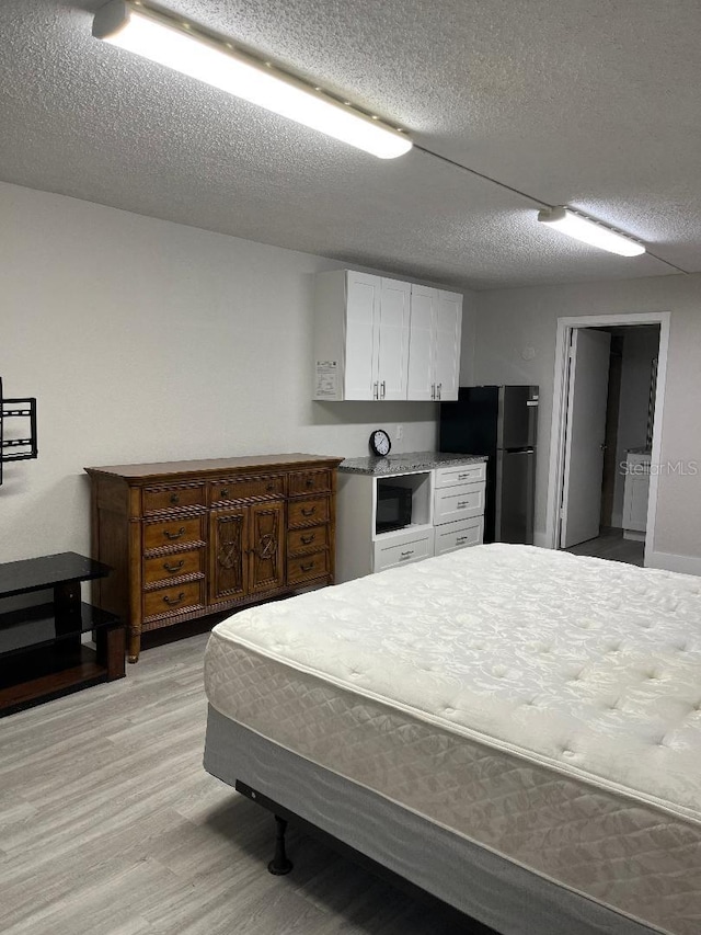 bedroom featuring light wood-type flooring, a textured ceiling, and stainless steel refrigerator