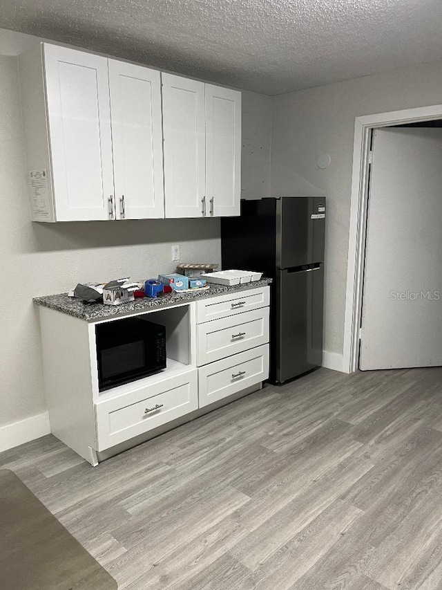 kitchen featuring light stone countertops, a textured ceiling, light hardwood / wood-style flooring, white cabinets, and fridge