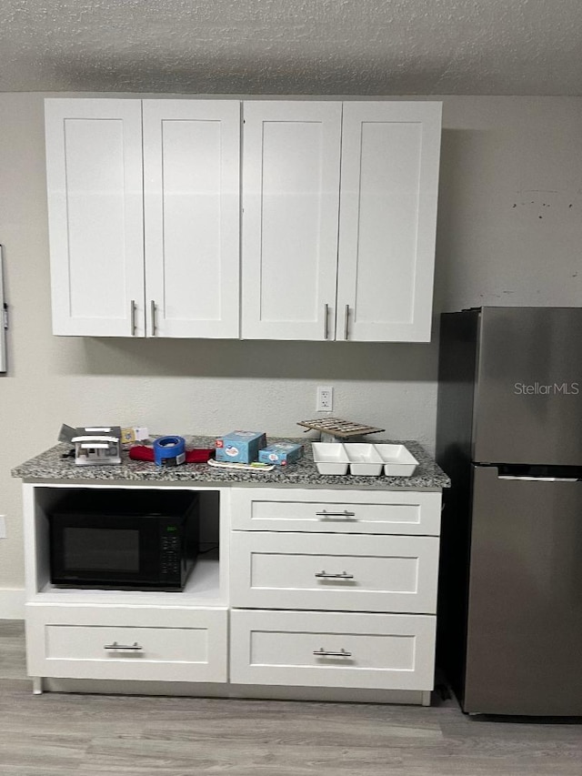 bar featuring white cabinetry, light stone countertops, light hardwood / wood-style flooring, stainless steel fridge, and a textured ceiling