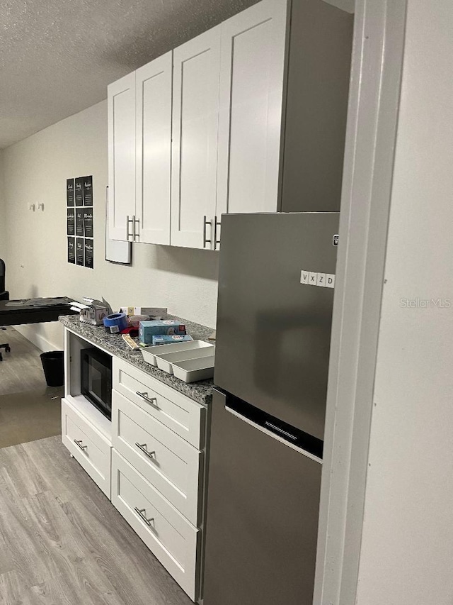 kitchen featuring stainless steel fridge, light wood-type flooring, a textured ceiling, dark stone countertops, and white cabinets