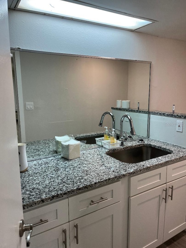 kitchen with white cabinets, a skylight, light stone countertops, and sink