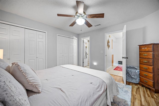 bedroom with ceiling fan, light hardwood / wood-style floors, a textured ceiling, and multiple closets