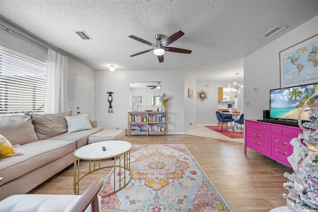 living room featuring a textured ceiling, ceiling fan with notable chandelier, and light hardwood / wood-style floors