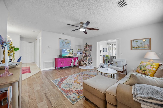 living room featuring ceiling fan, a textured ceiling, and light hardwood / wood-style flooring